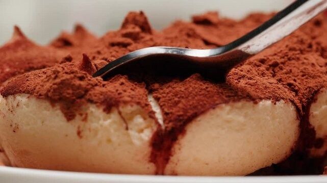Taking a little piece of traditional classic dessert tiramisu by spoon close-up. Popular Italian sweet tiramisu made of ladyfinger pastries and dipped in coffee, layered with a whipped mixture of eggs