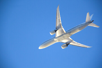 Underside view of a commercial airplane soaring through a clear blue sky