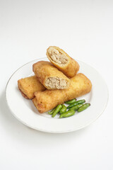 ‘Sosis solo’ or fried egg crepe with minced beef or chicken filling. This common Indonesia snack is served with chili pepper on white plate isolated in white background