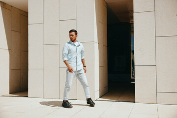 A confident man in casual light blue clothing stands in a modern architectural setting, looking into the distance.