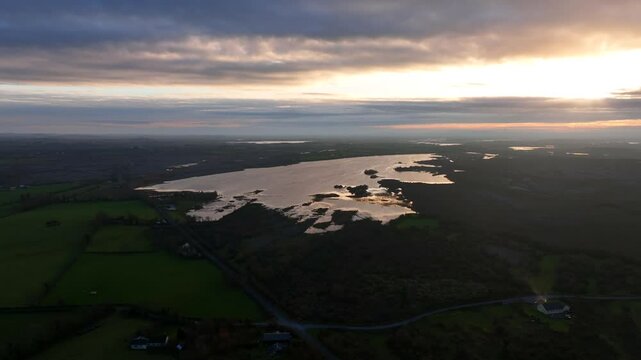 Lough Bunny, County Clare, Ireland, November 2023. Drone aerial overview at sunset perfectly establishing lake in the Burren as sun rays break between overcast skies.