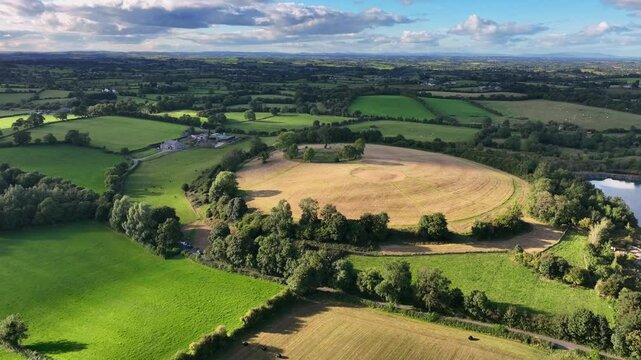 The Navan Fort, County Armagh, Northern Ireland, September 2022. Drone approaches knoll circular hilltop as cloud shadow passes down hillside at midday.