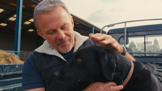 Close up of mature male farm worker sitting on tailgate of off road farm vehicle with working dog - shot in slow motion