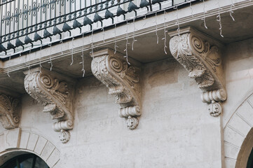 Brackets with raised wavy plant elements under an antique balcony with garland. Facade of an old...