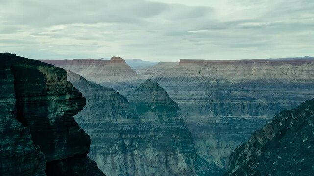 Majestic canyon reveals millennia of geological history. Wide-angle shot captures layered rock formations, showcasing nature's patient artistry in carving vast, rugged terrain under moody skies.	