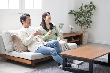 テレビや動画などを見るリビングでくつろぐ50代の夫婦の全身　話すカップルの正面の全身の広角