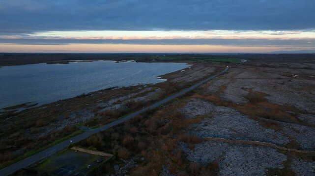 Lough Bunny, County Clare, Ireland, November 2023. Drone trucking pan left above empty road and ripples on shallow lake at blue hour.