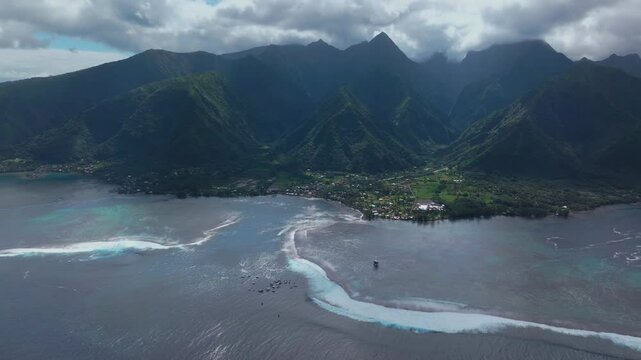 Coastal Teahupoo Tahiti aerial drone view perspective French Polynesia coral reef surf break waves mountains Pacific Ocean channel boats cloudy daytime Point Faremahora Pass Havae forward pan down