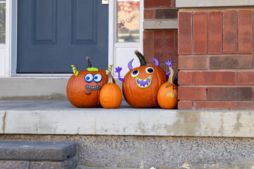 Autumn doorstep with three carved pumpkins - playful expressions - seasonal props against a brick wall. Taken in Toronto, Canada.