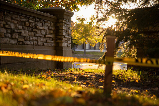 Golden-hour sunlight filters through trees &ndash; casting a warm glow on caution-taped wooden stake in grassy area &ndash; evoking mystery and caution in outdoor setting. Taken in Toronto, Canada.