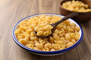 Raw macaroni pasta in bowl with spoon on wooden background, Food ingredient