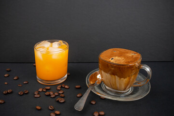 Home made dalgona coffee with coffee beans and a glass full of orange juice on black background