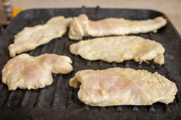 Cooking raw chicken breast on a black cast iron grill , soft focus close up