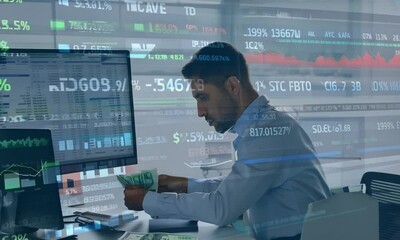  A man counting euros in front of a computer screen displaying stock prices, analyzing financial data - Powered by Adobe