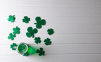Image of glass with green beer, clover and copy space on white wooden background © vectorfusionart