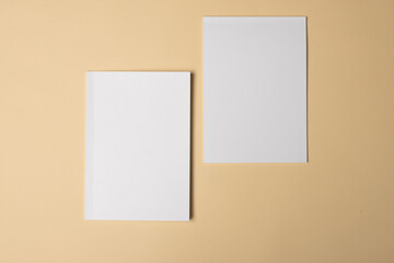 Two blank white sheets of paper lie on a beige surface with copy space