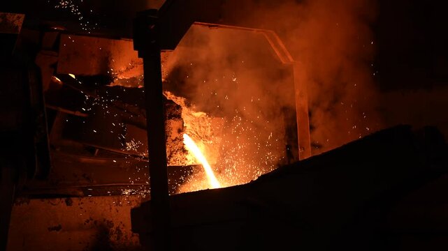 Operator pouring molten metal in automatic casting line in foundry factory, electric melting, high precision casting part manufacturing.  Molten metal pour from big container Into sand mold.
