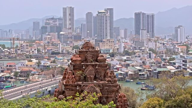 This footage captures the iconic Ponagar Temple set against the backdrop of the bustling city of Nha Trang, Vietnam. The ancient temple stands in the foreground and the modern city and a river behind