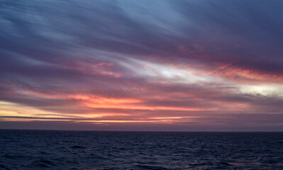 Colourful sunset over the sea, with purple and yellow sky, and calm water. 