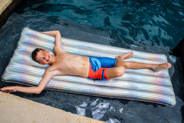 Laughing carefree young boy floating happily on an inflatable pool raft in his backyard swimming pool © 3Days2Go Media