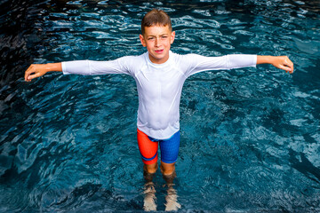 Soaking wet young boy standing in his backyard swimming pool, arms out, ready to back flop into the...