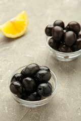 Black olives with lemon on grey concrete background. Vertical photo