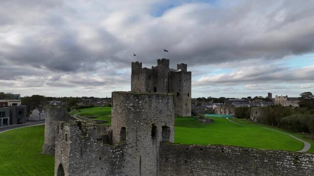Trim Castle, County Meath, Ireland, October 2023. Drone orbits clockwise sweeping low past the imposing Medieval curtain wall fortifications and pulls away ascending to an elevated aerial view.