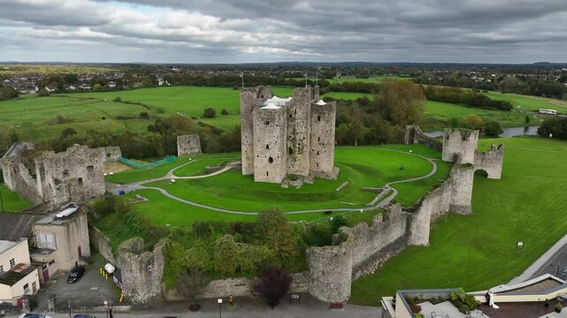 Trim Castle, County Meath, Ireland, October 2023. Drone orbits clockwise above buildings and road keeping the Medieval Fortress ruins centered on overcast even lighting day.