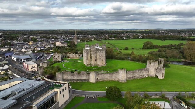 Trim Castle, County Meath, Ireland, October 2023. Drone slowly orbits counter clockwise, with an elevated view of the imposing Medieval Fortress on cloudy day, nearby river Boyne and town panorama.
