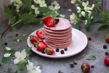 Delicious breakfast setting with a stack of homemade berry pancakes topped with fresh strawberries and cream. The vibrant colors and flowers create an appetizing and inviting summer morning scene
