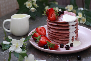 Delicious breakfast setting with a stack of homemade berry pancakes topped with fresh strawberries and cream. The vibrant colors and flowers create an appetizing and inviting summer morning scene