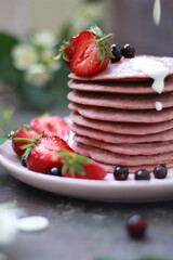 Delicious breakfast setting with a stack of homemade berry pancakes topped with fresh strawberries and cream. The vibrant colors and flowers create an appetizing and inviting summer morning scene