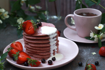 Delicious breakfast setting with a stack of homemade berry pancakes topped with fresh strawberries and cream. The vibrant colors and flowers create an appetizing and inviting summer morning scene