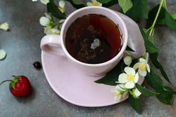 An elegant pink cup filled with aromatic tea, surrounded by jasmine flowers and fresh berries of strawberry and blackcurrant, creates an atmosphere of morning coziness and tranquility.