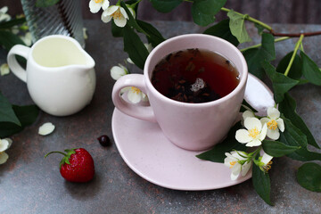 An elegant pink cup filled with aromatic tea, surrounded by jasmine flowers and fresh berries of strawberry and blackcurrant, creates an atmosphere of morning coziness and tranquility.