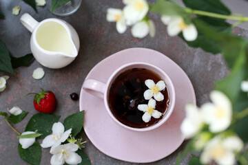 An elegant pink cup filled with aromatic tea, surrounded by jasmine flowers and fresh berries of strawberry and blackcurrant, creates an atmosphere of morning coziness and tranquility.