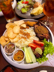 mixed fried and grilled chicken rice, traditional indonesian cuisine called nasi campur comprise of fried or grilled chicken served with local salad and chili paste and also crackers, delicious