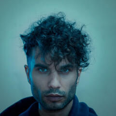 Portrait of a man with curly hair under blue lighting, exuding a mysterious and intense expression