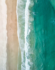 Aerial view of turquoise water and waves crashing onto a sandy beach