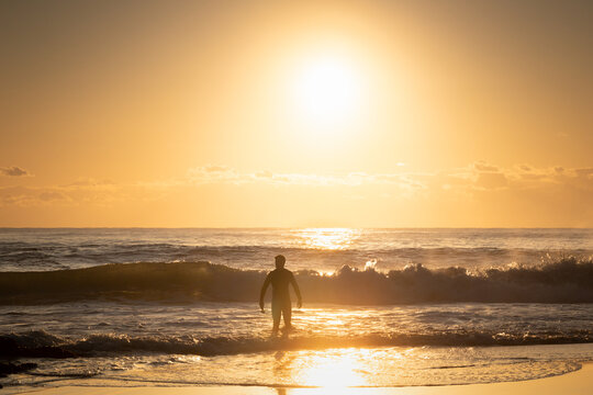 Silhouette man walks into waves at ocean golden sunrise