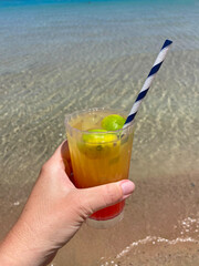 Cocktail in glass width some lemon into the hand on see background. Holiday and relaxing concept
