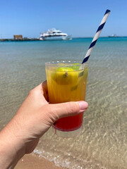Cocktail in glass width some lemon into the hand on see background. Holiday and relaxing concept