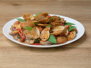 Stir fried striped clams with basil, chilli paste, garlic and fresh chilies. Placed in a white plate with a beautiful pattern and on the wood pattern background.