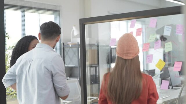 A team of developers are currently discussing the feasibility of the project. By writing and pasting work on the glass. Showcasing ideas from an international team in a bright modern conference room.