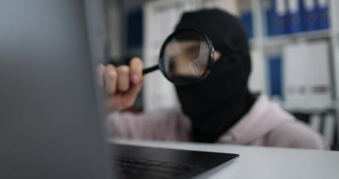 Internet stealing masked person looks at computer screen with magnifying glass. Internet fraud and cybercrime concept