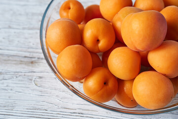 Ripe apricots in a glass bowl on a white wooden background.