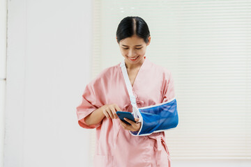 A young Asian female wearing a pink patient uniform stands isolated against a white wall...