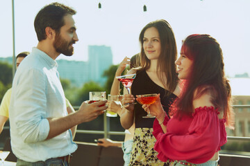 Portrait of group of friends enjoys bright outdoor gathering, their glasses meeting in celebratory toast. Concept of party, Friday mood, celebration, summer holidays, relax.