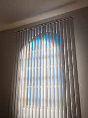 Standard closed beige vertical blinds as a detail of the bedroom interior.