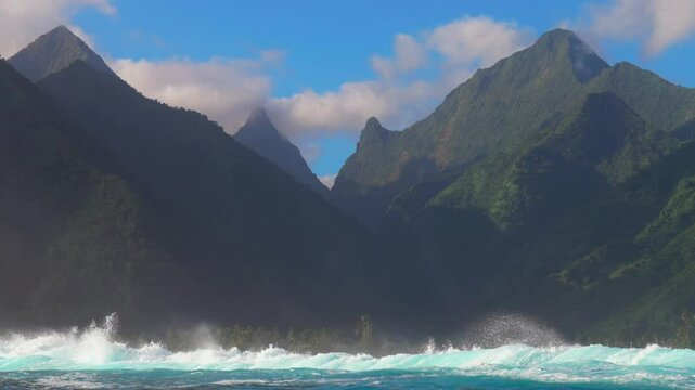 Surfing surf barrel waves Teahupoo Tahiti French Polynesia crashing swell on shallow coral reef South Pacific island towering mountain peaks ocean waterhousing landscape blue sky super slow motion